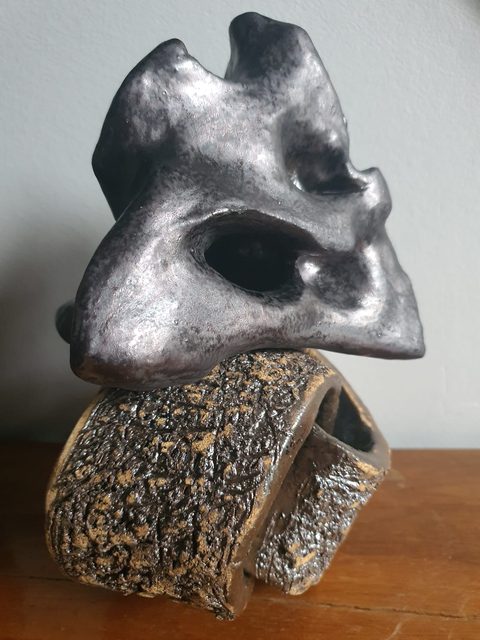 Srebrzysta rzeźba ceramiczna w kształcie maski na fakturowanym pierścieniu